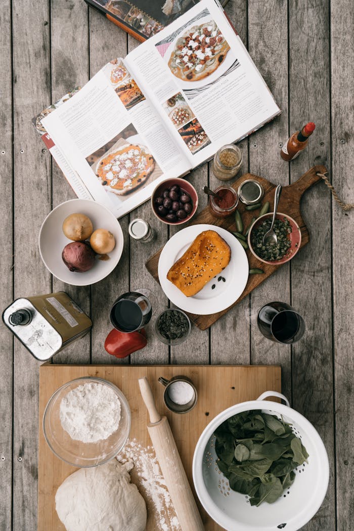 Overhead view of ingredients for pizza making with an open cookbook. Perfect for cooking enthusiasts.