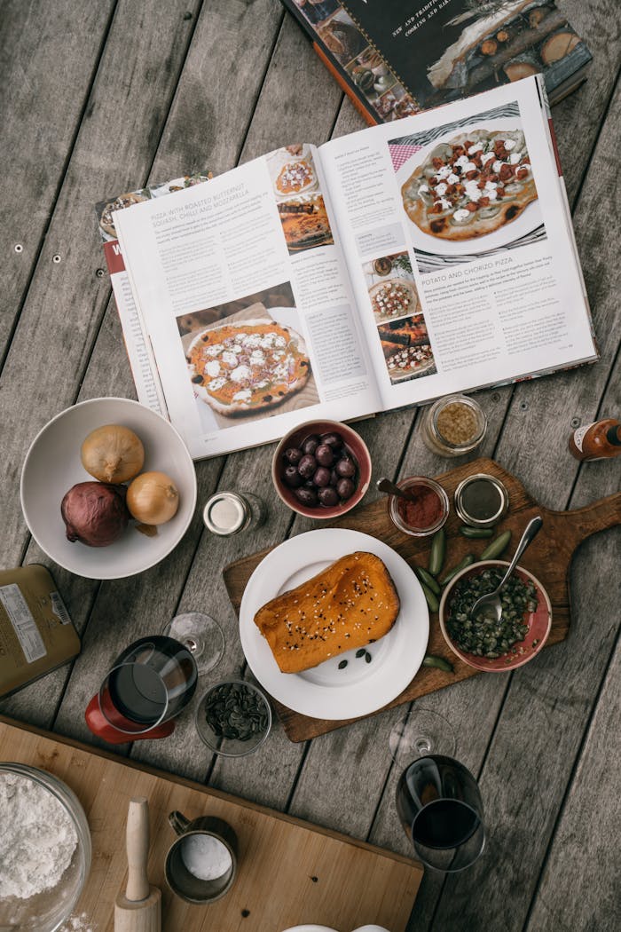 Flat lay showing a variety of cooking ingredients and an open cookbook on a rustic wooden table.